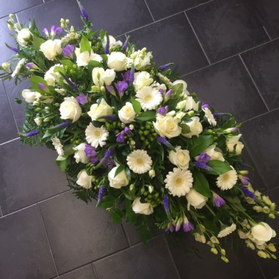 Purple & White Casket Spray - A classic Purple & White casket spray. White Roses, White Eustomia, Gerbras, Lime Green Viburnham, Hydrangeas and Carnations are interspersed with purple Lisianthus beautifully presented on a bed of luscious green foliage.

Image Shown is Luxury 5ft

Please note this item is only suitable for delivery to a funeral. Please make a selection from an alternative range, if you would like to express your sympathy to the bereaved. Product photography is indicative of the highest price point. Please note that seasonal availability of individual stems may vary from those in the picture. Our professional florist may substitute flowers for a suitable alternative, similar in style, colour, quality and value. Where flower designs include a sundry item such as a vase or basket it may not always be possible for our florists to include the exact item pictured. Every effort will be taken to ensure that the item is substituted for a similar design.Price above includes delivery charge but excludes relay fee.