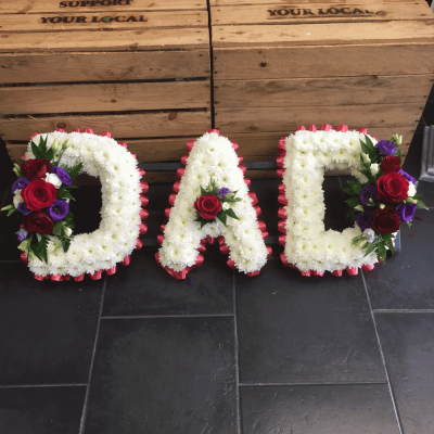 DAD Letters - Beautiful white Chrysanthemums with a flourish of red Roses and purple Eustomia, edged with red ribbon pleats, form the name DAD. Stand included.

Please note this tribute is availble in several colour choices, please advise when placing your order.

Purple, Lilac, Purple, Yellow, Cream. Blue, Orange, Red

Please note this item is only suitable for delivery to a funeral. Please make a selection from an alternative range, if you would like to express your sympathy to the bereaved. Product photography is indicative of the highest price point. Please note that seasonal availability of individual stems may vary from those in the picture. Our professional florist may substitute flowers for a suitable alternative, similar in style, colour, quality and value. Where flower designs include a sundry item such as a vase or basket it may not always be possible for our florists to include the exact item pictured. Every effort will be taken to ensure that the item is substituted for a similar design.Price above includes delivery charge but excludes relay fee.