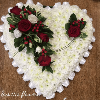 Based White Heart - A beautiful white based heart with a ribbon pleated edging, Red Rose and Viburnum corsarge alongside variegated pitto and lime Dracaena, hypericum, Chinna grass and ming fern complete this stunning arrangement.