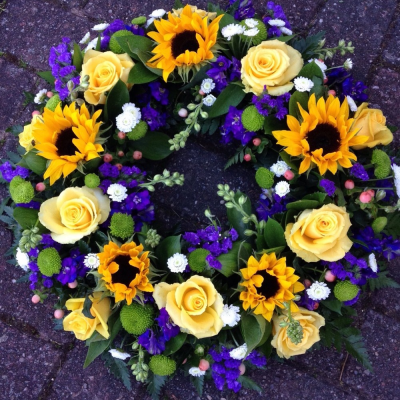 Sunflower Wreath - A beautiful white, purple & Lemon, Traditional Wreath. Sunflowers, yellow roses, statice and Eustomia sit perfectly alongside variegated china grass and lime foliages,,

Available in other colours please advise when ordering.